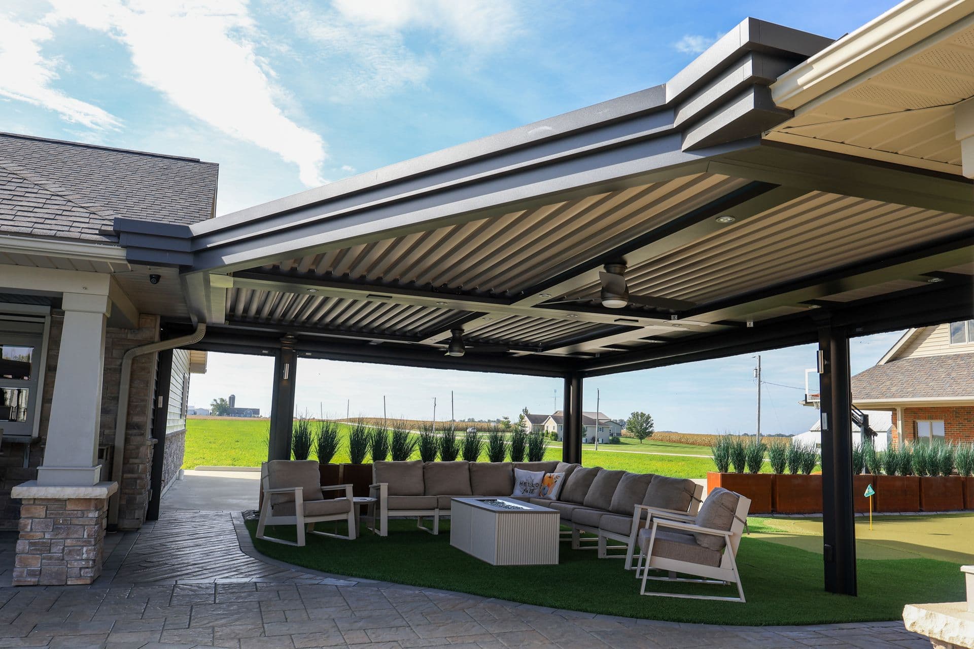 Modern backyard patio with retractable louvered pergola, outdoor seating area with sectional sofa and fire pit, overlooking rural landscape