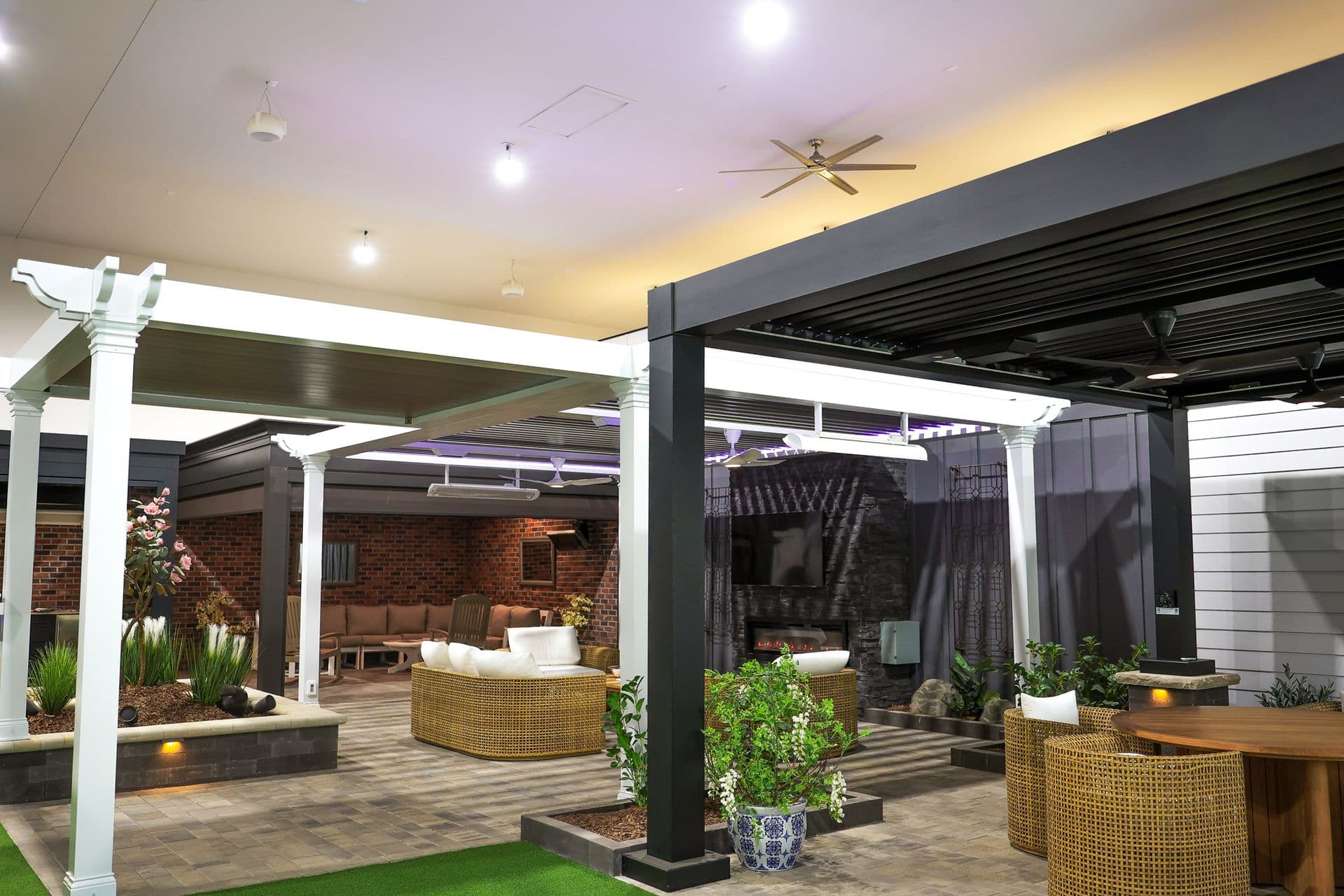 Modern outdoor living space showroom displaying pergolas, lounge furniture, ambient lighting, and landscaping with brick backdrop and decorative plants