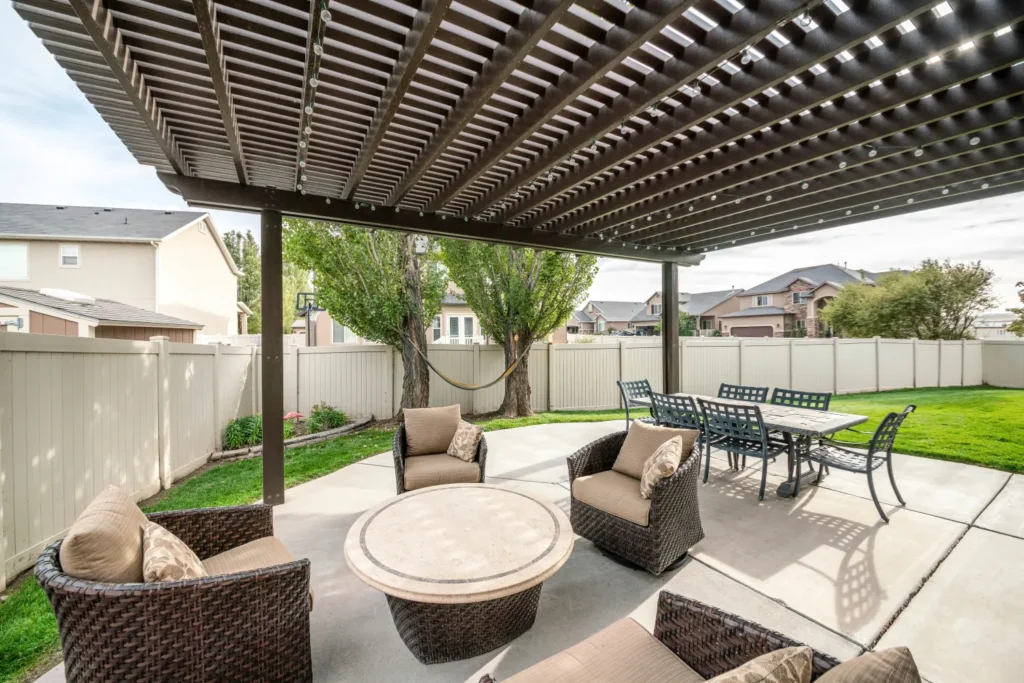 Backyard lattice patio enclosure with a dark wood pergola overhead, providing partial shade to a cozy seating area and outdoor dining set—an elegant and functional option for partial sun protection in 2024.